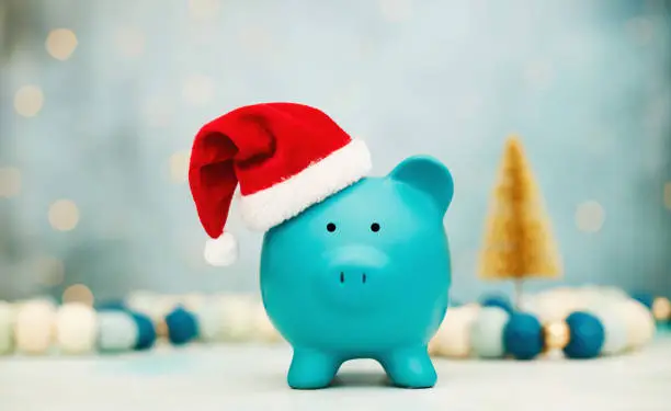 Photo of Teal piggy bank wearing Santa hat with Christmas decorations background. Christmas savings or spending theme