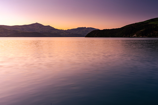 This October 2021 long-exposure dusk image shows Akaroa Harbour in Ōtautahi Christchurch, Aotearoa New Zealand. The harbour flows out to Te Moana-nui-a-Kiwa Pacific Ocean. This area is part of Horomaka Banks Peninsula, an ancient volcanic complex.