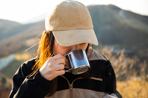 A close up portrait of a Japanese woman drinking a cup of coffee or tea in the mountains.