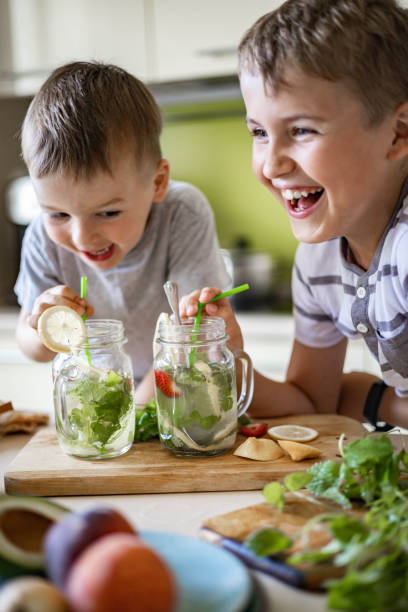 zwei lachende kleine jungen trinken erfrischenden vitamin sommercocktail aus glas mit strohhalm spaß haben - vitamin enriched stock-fotos und bilder