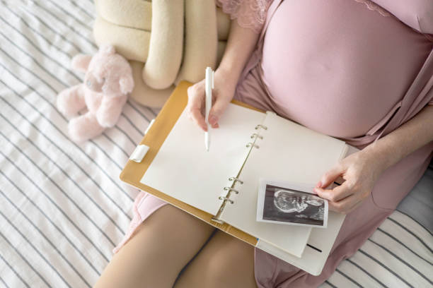 istock Top view caring future mother writing diary with ultrasound x ray photo sitting on comfortable bed 1354801046