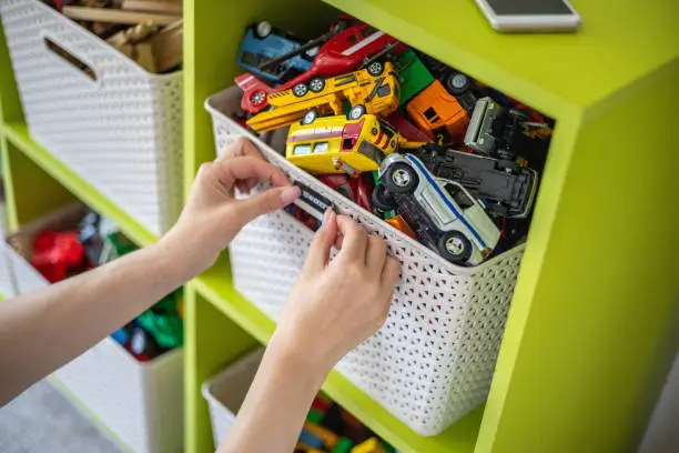 Woman hands applying printing sticker with name title of children toys for comfortable sorting and storage at home. Caring mother organizing domestic space for kids. Housekeeping and household