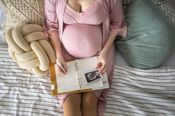 istock Top view caring future mother writing diary with ultrasound x ray photo sitting on comfortable bed 1354801847