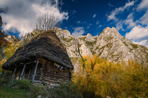 Small rural barn hut against an imposing rocky mountain with a beautiful blue sky and clouds