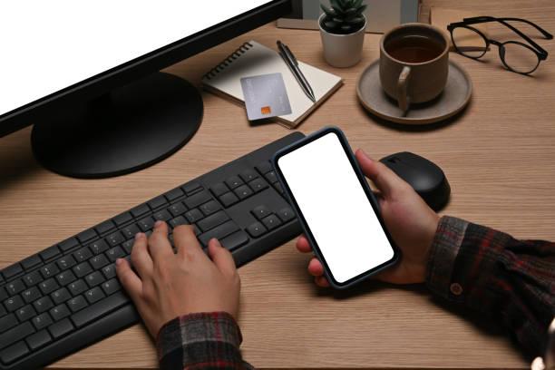 istock Cropped shot man holding smart phone and and working with computer at home office. 1354805987