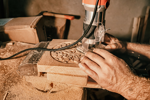 A carpenter craftsman carves wood using an automated tool according to a previously prepared pattern. Close-up on skill hands at work