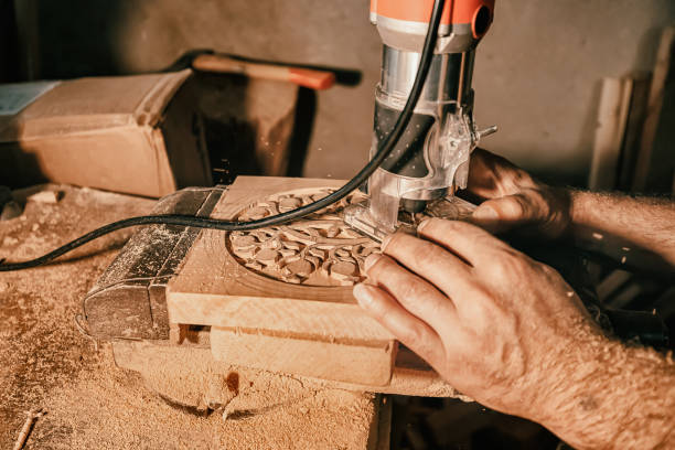 A carpenter craftsman carves wood using an automated tool according to a previously prepared pattern. Close-up on skill hands at work A carpenter craftsman carves wood using an automated tool according to a previously prepared pattern. Close-up on skill hands at work carving craft activity stock pictures, royalty-free photos & images