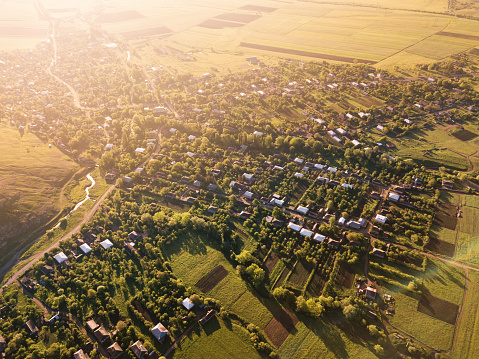 Panoramic aerial view of green and plowed agricultural fields and several village houses illuminated by the rising sun