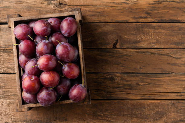 istock Tasty plums in box on rustic wooden background with copyspace. Top view 1354814033