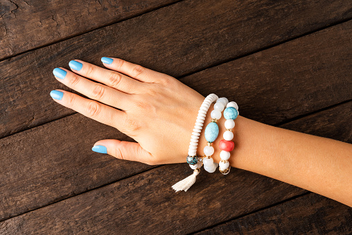 Woman’s hand with blue nails and jewelry on wooden background. Top view