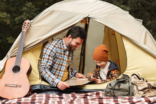 istock Father and little son reading map and using compass while sitting in touristic tent at campsite 1354817218