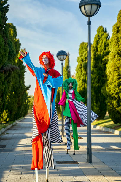istock Creative clowns on stilts walking on pathway in sunny park 1354819122