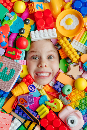 Little girl lying on the background of various colourful plastic and wooden toys. Childhood concept. Top view, flat lay.