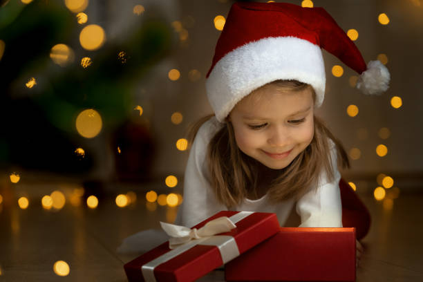 istock Little girl opens box with light at dark next to christmas tree. 1354820721
