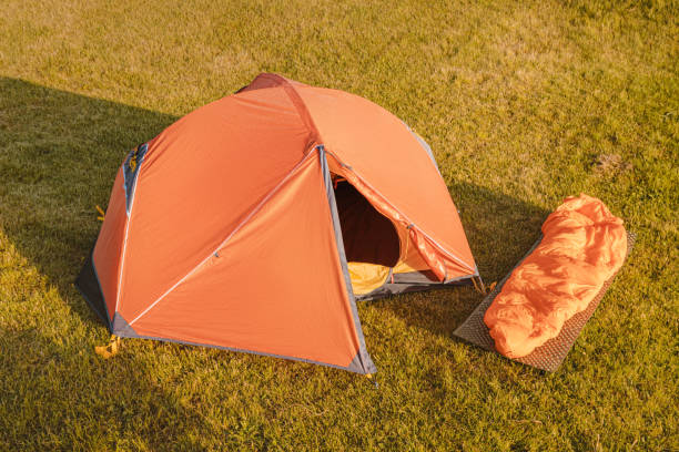 istock Hiking equipment - a modern orange arc tent and a rug with a warm down sleeping bag 1354820738