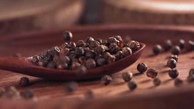 Black pepper falling on a wooden spoon.Slow motion. Close up