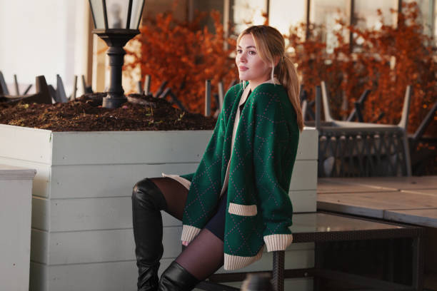 Beautiful Woman thinking or waiting. Stylish fashion model wearing oversize green sweater, shorts, looking away. Background autumn leaves, depth field Beautiful Woman thinking or waiting. Stylish fashion model wearing oversize green sweater, shorts, looking away. Background autumn leaves and depth field cardigan sweater stock pictures, royalty-free photos & images