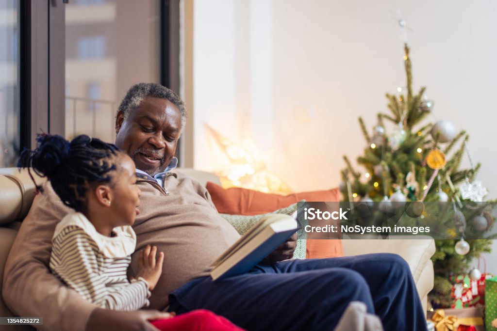 Christmas night with a grandfather and a fairytale book Grandfather and granddaughter reading book. Christmas time Christmas Stock Photo
