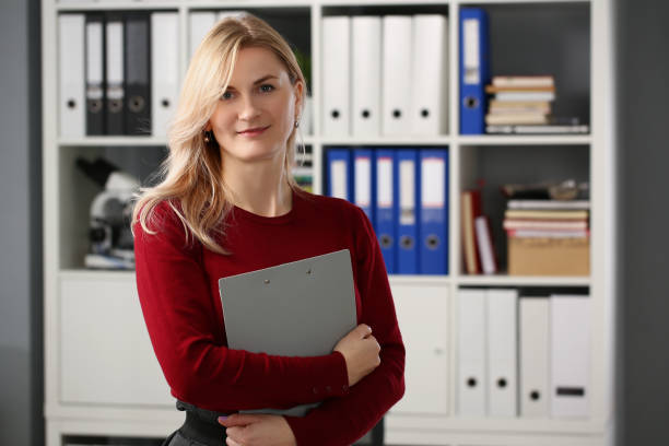 istock Cute blonde young office worker with documents posing in stylish outfit 1354828983