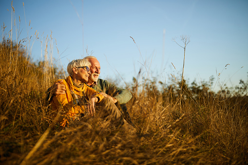 Embraced mature couple enjoying while relaxing in tall grass during autumn day in nature. Copy space.