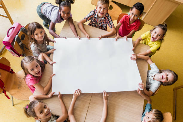 Above view of happy elementary students with blank paper in the classroom.