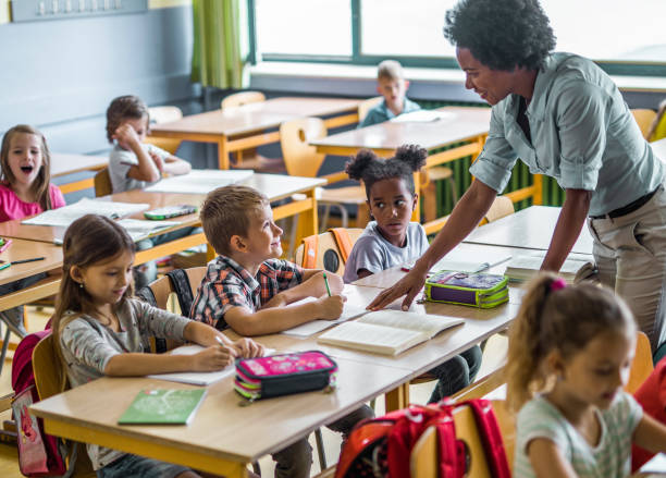 istock Happy black teacher talking to school kids on a class at elementary school. 1354835045