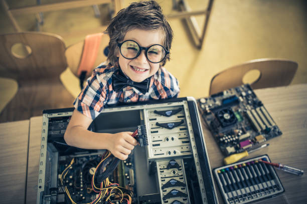 istock Above view of nerdy elementary student repairing electrical components of a computer in the classroom. 1354835278