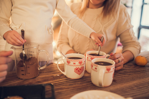 Family: mom, dad and daughter in white sweaters cook and drink cocoa with marshmallows. Closeup hands and cups. Christmas concept.