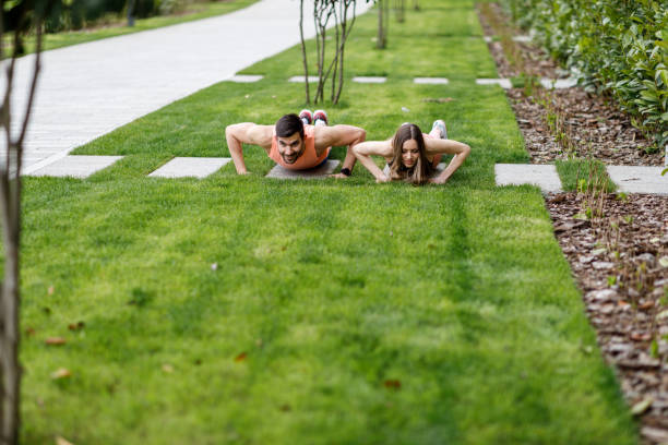 um jovem casal está fazendo flexões em um campo gramado. - pilates women sit ups yoga - fotografias e filmes do acervo