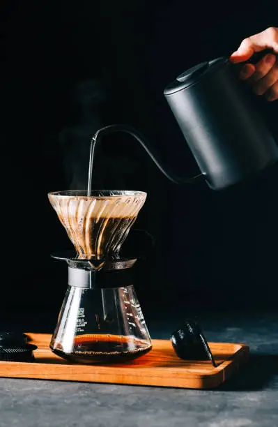 Alternative coffee brewing method, using pour over dripper and paper filter. Black background