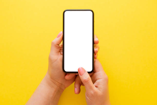 istock Person holding blank mobile phone in both hands on yelloe background 1354838396