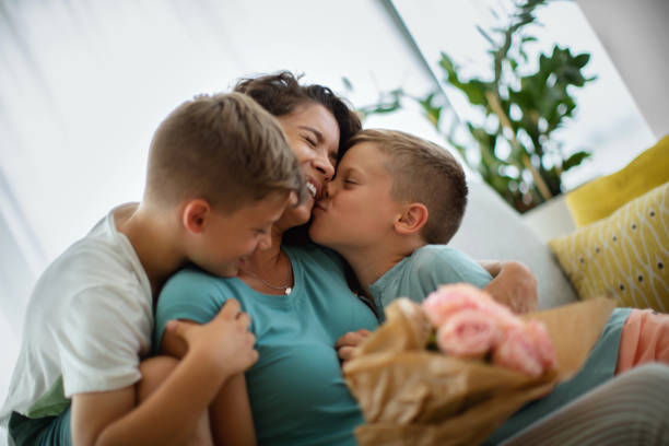 Mother's day. Sons hugging and kissing their mother and giving her a bouquet of roses for Mother's Day. cheek photos stock pictures, royalty-free photos & images