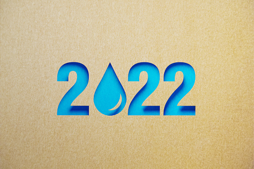 Cut out water droplet shape made of recycled paper forming 2022 on blue background. Horizontal composition with copy space. Sustainability and clean water concept.