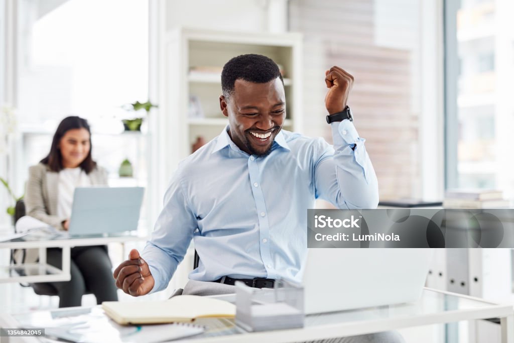 Shot of a young businessman cheering while working on a laptop in an office Everyone knows how great winning feels Ecstatic Stock Photo