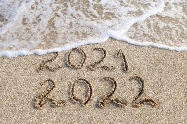istock 2021, 2022 years written on sandy beach sea. Wave washes away 2021. 1354842079
