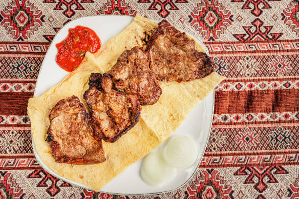 istock Fried fresh meat on thin pita bread or lavash and a tablecloth with ethnic national patterns. 1354846382