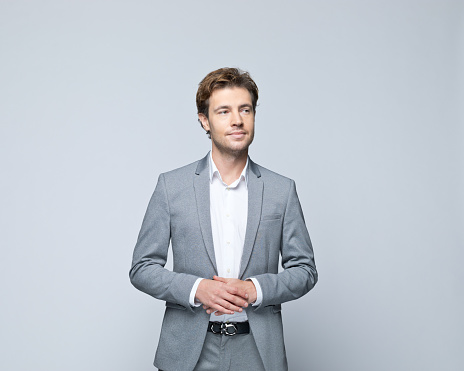 Portrait of handsome young man wearing grey jacket, looking away. Studio shot of male entrepreneur against grey background.
