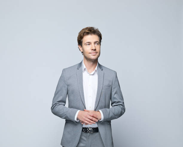 Portrait of confident young businessman Portrait of handsome young man wearing grey jacket, looking away. Studio shot of male entrepreneur against grey background. business man looking away stock pictures, royalty-free photos & images