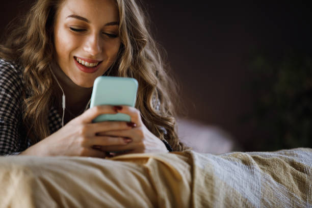 headshot di un'allegra adolescente che si rilassa sul letto, usando lo smartphone e ascoltando musica - one teenage girl only on the phone bed lying on front foto e immagini stock