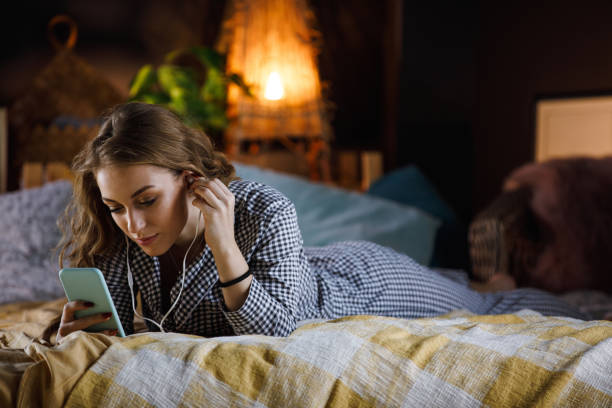 ragazza adolescente sdraiata sul letto e ascoltando musica mentre si utilizza lo smartphone - one teenage girl only on the phone bed lying on front foto e immagini stock