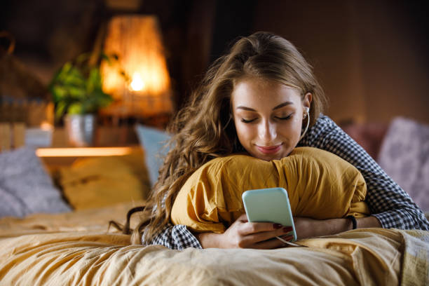 ragazza adolescente sdraiata sul suo letto accogliente, ascoltando musica e usando lo smartphone - one teenage girl only on the phone bed lying on front foto e immagini stock