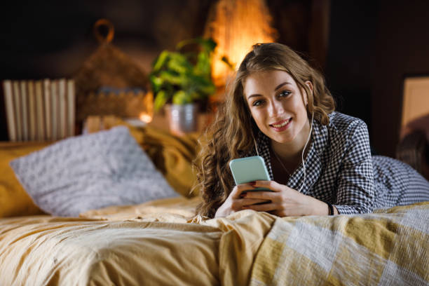 adolescente alegre sorrindo para a câmera enquanto ouvia música e relaxa - one teenage girl only on the phone bed lying on front - fotografias e filmes do acervo