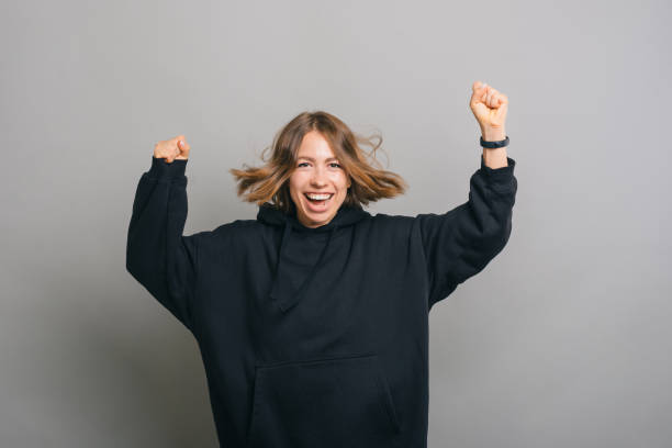 istock A happy woman is jumping with both her hands up while smiling at the camera 1354853072