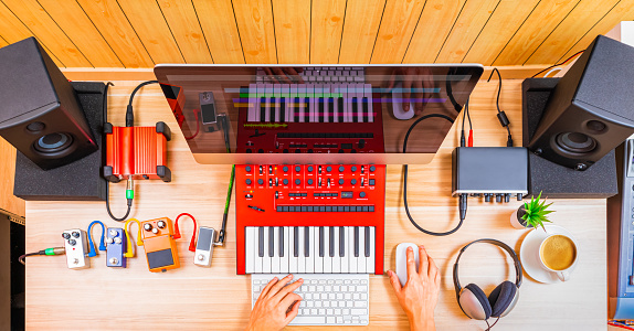 top view of professional music producer, composer hands arranging music on computer and recording equipments on desk. music production technology, home studio concept