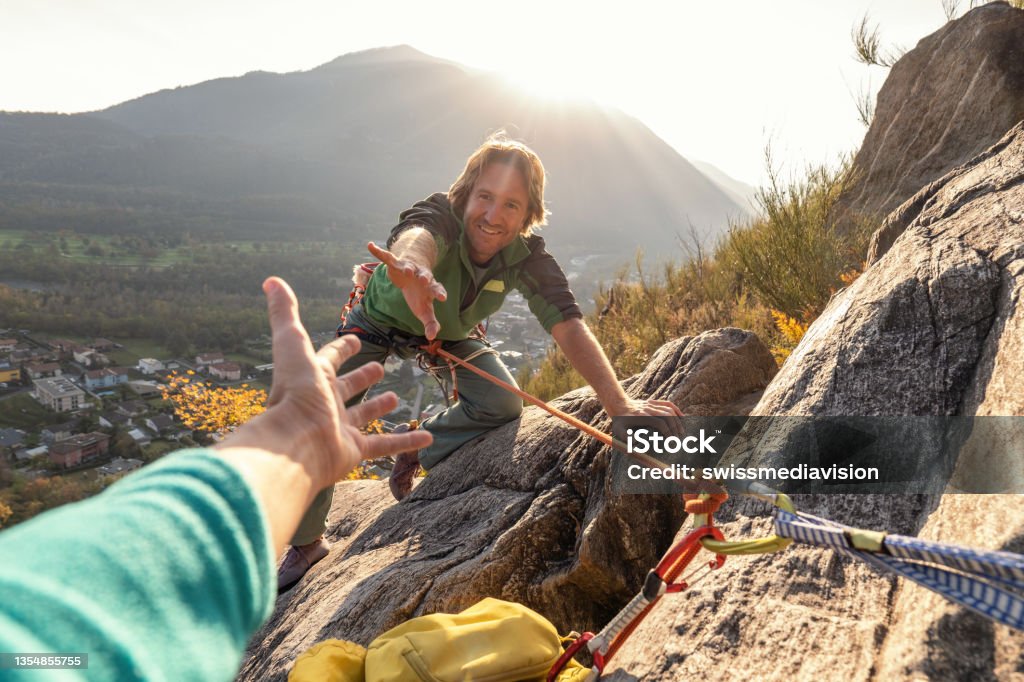 Male rock climber reaches his hand out to ask for assistance Male rock climber reaches for rock summit Rock Climbing Stock Photo