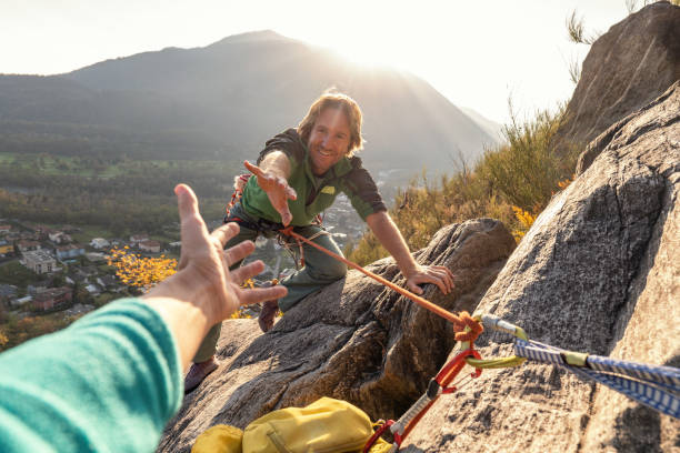alpinista macho estende a mão para pedir ajuda - hanging on rock rock climbing - fotografias e filmes do acervo