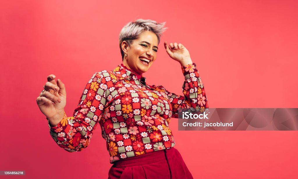 Feeling vibrant and energetic Feeling vibrant and energetic. Happy young woman dancing and smiling cheerfully while standing against a red background. Young woman with dyed hair having fun in the studio. Women Stock Photo