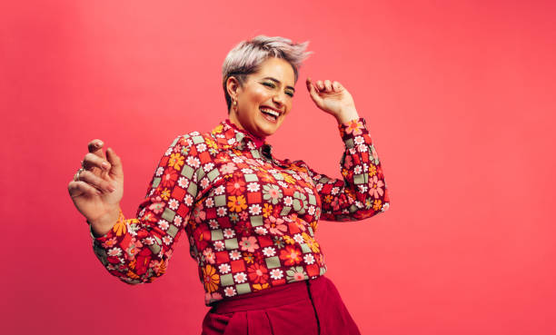 Feeling vibrant and energetic Feeling vibrant and energetic. Happy young woman dancing and smiling cheerfully while standing against a red background. Young woman with dyed hair having fun in the studio. vibrant color stock pictures, royalty-free photos & images