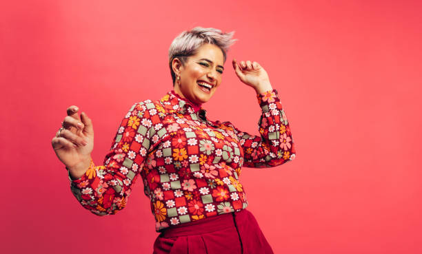 Feeling vibrant and energetic Feeling vibrant and energetic. Happy young woman dancing and smiling cheerfully while standing against a red background. Young woman with dyed hair having fun in the studio. confidence stock pictures, royalty-free photos & images