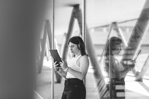 Beautiful caucasian girl student holding a tablet and listening with headphones in the campus.  Learning and education concept. Monochrome version.